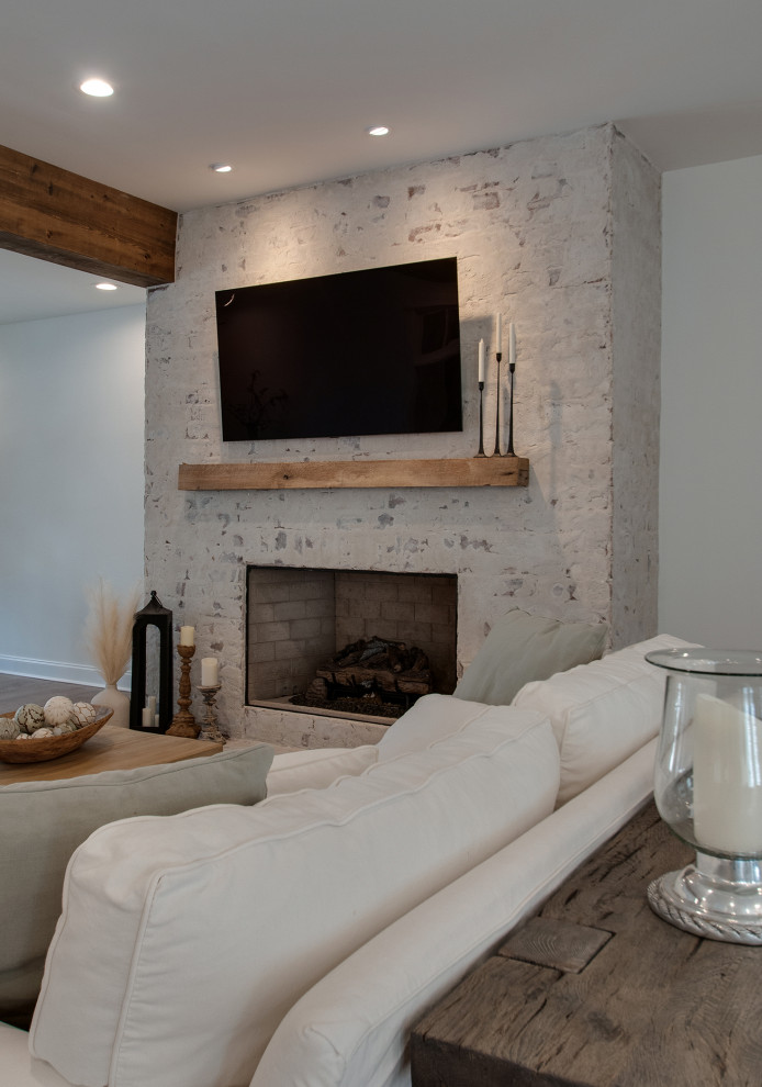 ナッシュビルにある高級な中くらいなカントリー風のおしゃれなLDK (白い壁、無垢フローリング、レンガの暖炉まわり、壁掛け型テレビ、白い床、表し梁) の写真