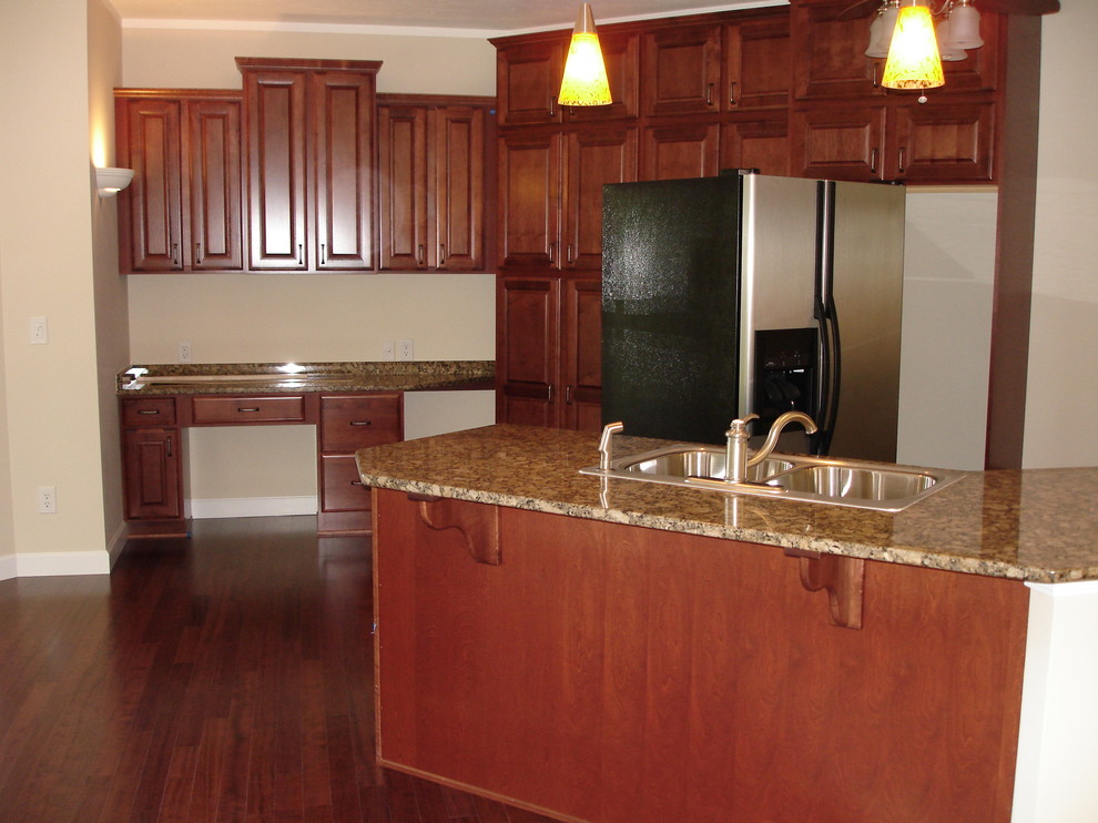 Example of a medium tone wood floor kitchen design with a double-bowl sink, medium tone wood cabinets, granite countertops, stainless steel appliances and a peninsula