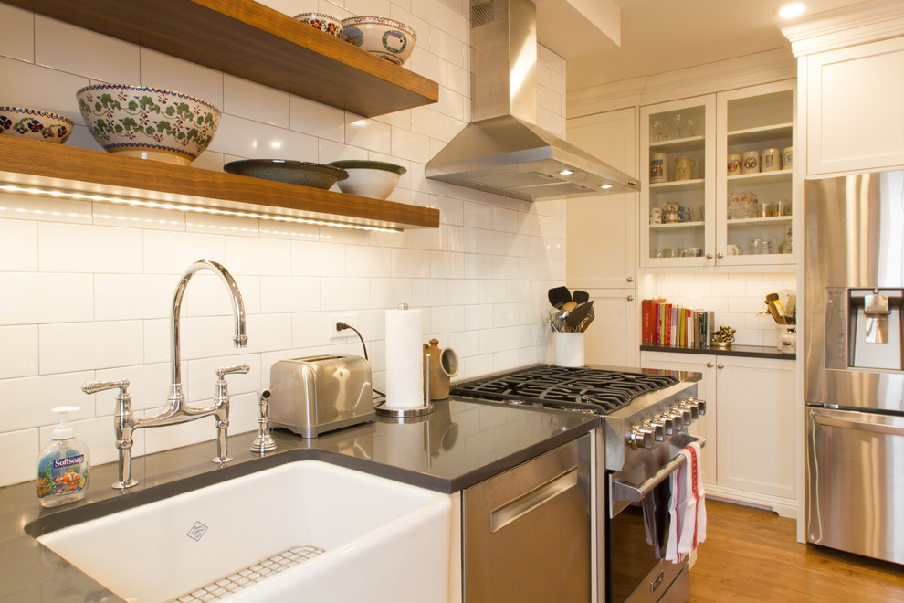Example of a light wood floor kitchen design in Chicago with a farmhouse sink, white cabinets, quartzite countertops, white backsplash, subway tile backsplash, stainless steel appliances and an island