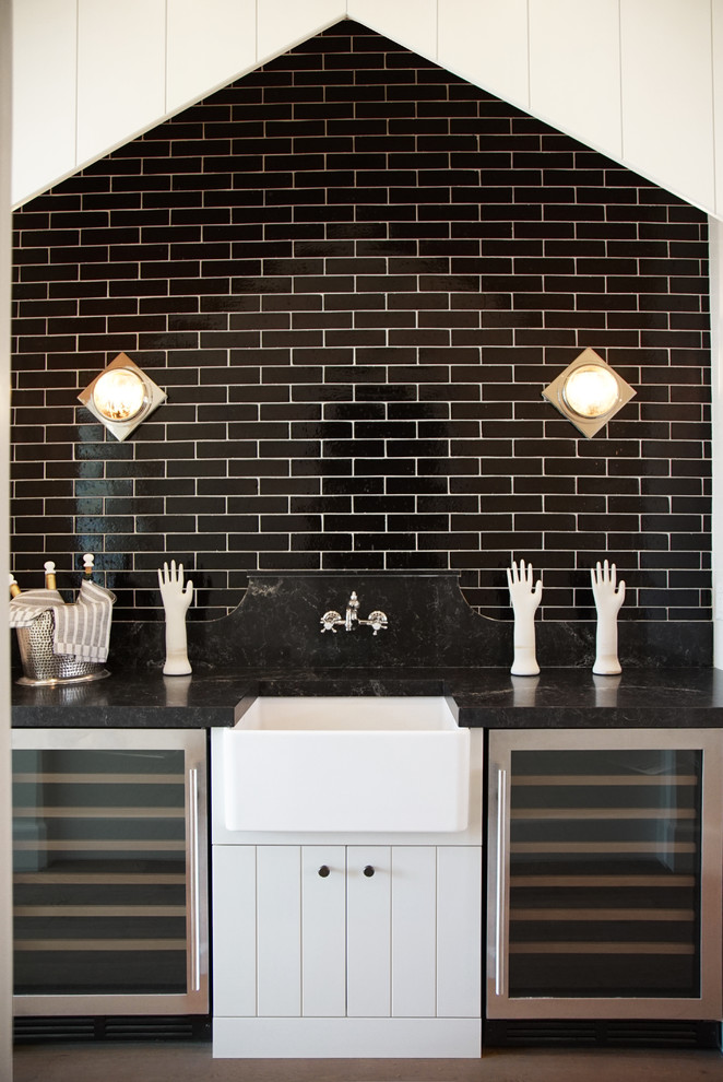 This is an example of a small transitional single-wall wet bar in Phoenix with flat-panel cabinets, white cabinets, quartz benchtops, black splashback, brick splashback, medium hardwood floors, brown floor and black benchtop.