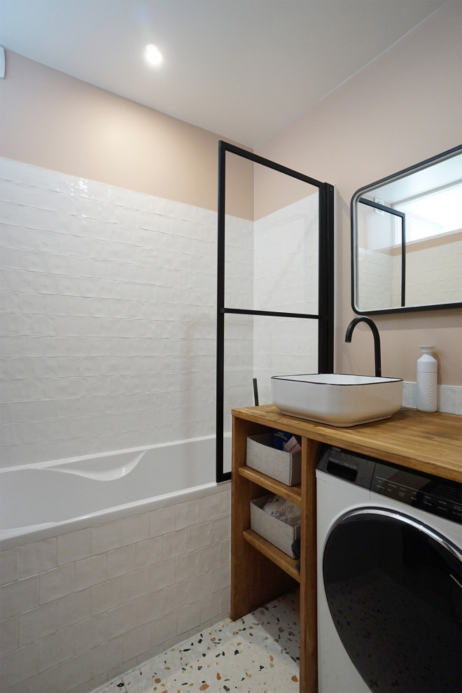 Bild på ett litet funkis beige beige badrum för barn, med ett undermonterat badkar, en dusch/badkar-kombination, vit kakel, keramikplattor, rosa väggar, terrazzogolv, ett nedsänkt handfat, träbänkskiva och flerfärgat golv