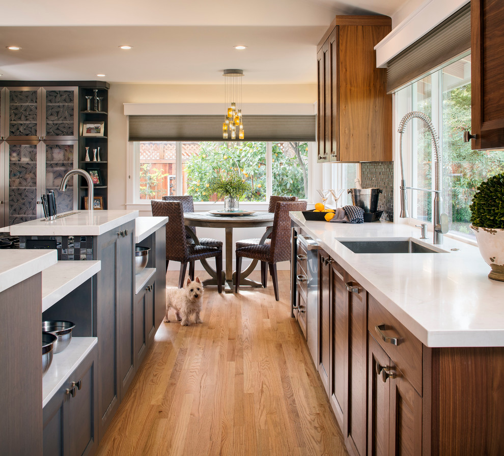 Example of a transitional galley light wood floor eat-in kitchen design in Sacramento with an undermount sink, shaker cabinets, medium tone wood cabinets, quartz countertops, black backsplash, glass tile backsplash, stainless steel appliances and an island