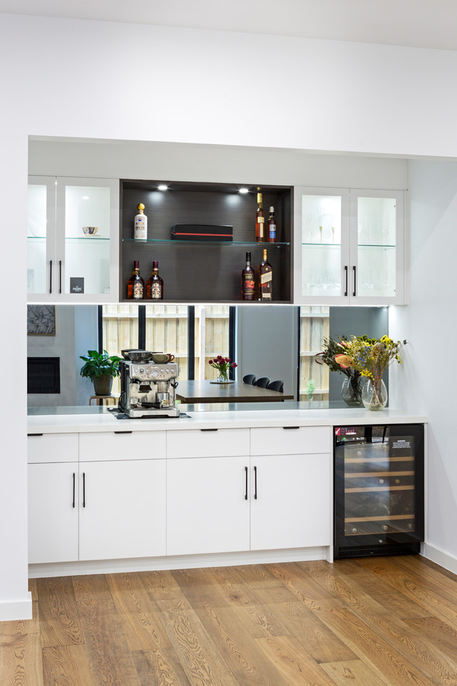Photo of a mid-sized contemporary single-wall eat-in kitchen in Melbourne with an undermount sink, flat-panel cabinets, white cabinets, marble benchtops, grey splashback, mirror splashback, black appliances, medium hardwood floors, with island, multi-coloured floor and white benchtop.