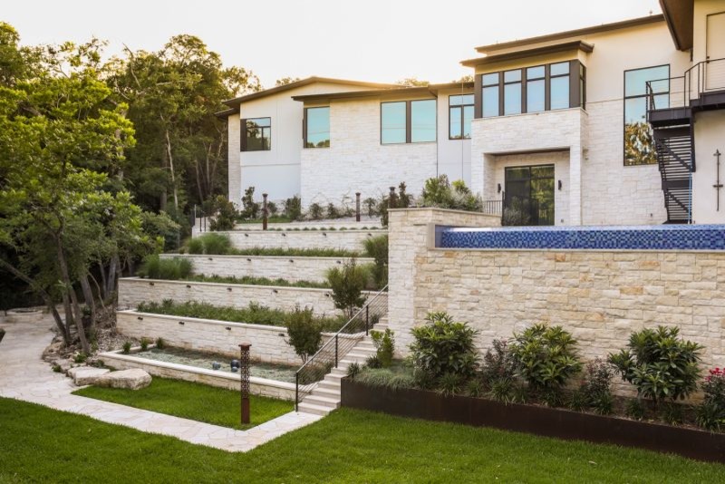 This is an example of a large modern sloped garden in Austin with a retaining wall.