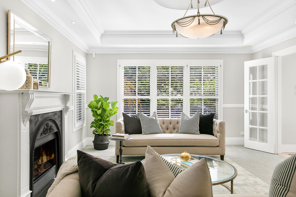 Photo of a mid-sized transitional formal enclosed living room in Sydney with grey walls, carpet, a standard fireplace, a plaster fireplace surround, beige floor and coffered.