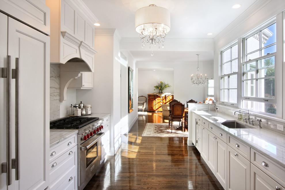 Photo of a traditional galley eat-in kitchen in New York with an undermount sink, recessed-panel cabinets, white cabinets, marble benchtops, grey splashback, panelled appliances, medium hardwood floors and marble splashback.