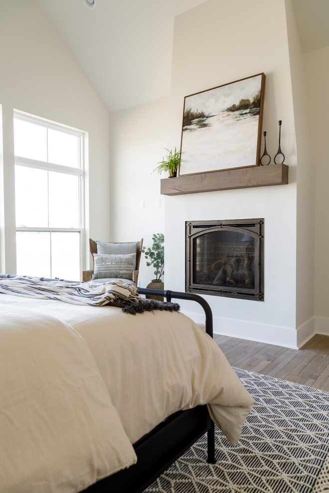 Cette photo montre une chambre parentale nature de taille moyenne avec un mur blanc, un sol en bois brun, une cheminée standard, un manteau de cheminée en plâtre, un plafond voûté et du lambris.