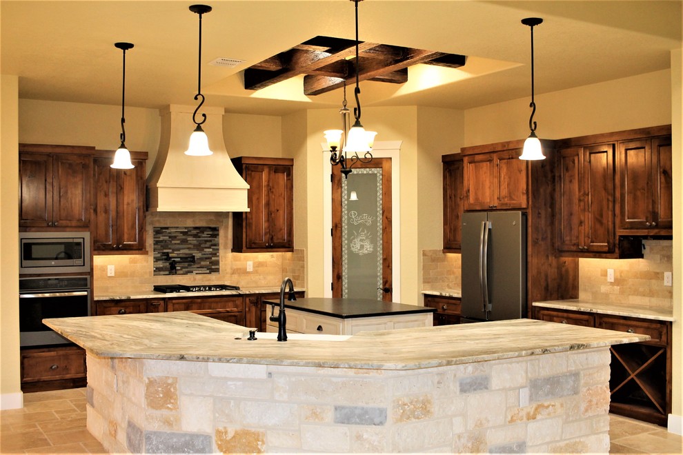Photo of a large country u-shaped eat-in kitchen in Other with a farmhouse sink, raised-panel cabinets, dark wood cabinets, granite benchtops, beige splashback, travertine splashback, stainless steel appliances, travertine floors, with island, beige floor and grey benchtop.