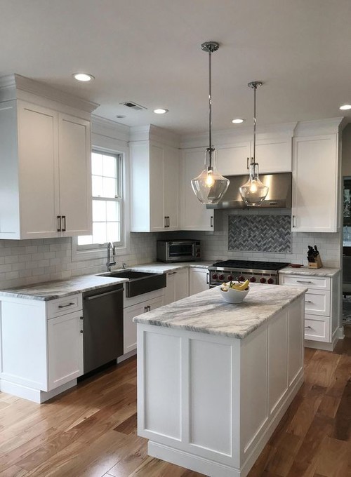White Shaker kitchen cabinets in Montreal with marble-look quartz, subway tile backsplash, island, glass pendants, and stainless appliances