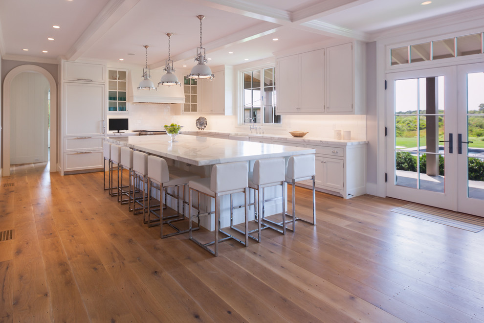 This is an example of a large beach style l-shaped open plan kitchen in Boston with a farmhouse sink, glass-front cabinets, white cabinets, marble benchtops, white splashback, ceramic splashback, stainless steel appliances, medium hardwood floors and with island.