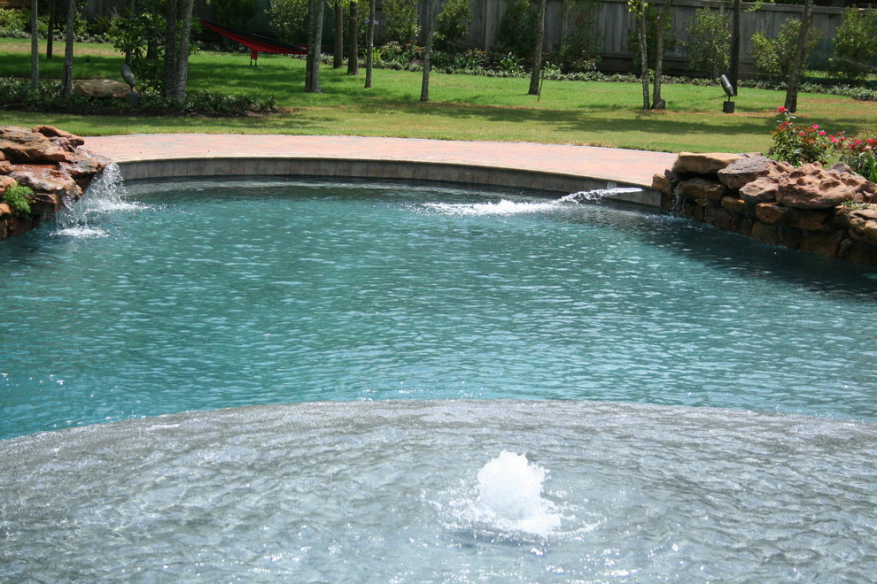 This is an example of a large tropical backyard custom-shaped natural pool in Austin with a hot tub and brick pavers.