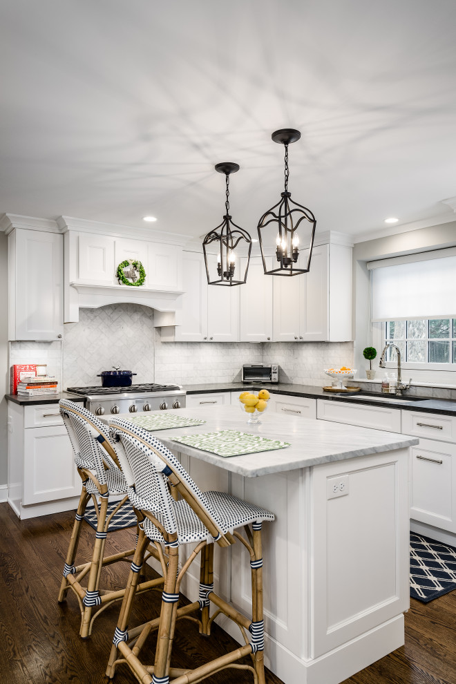 This is an example of a mid-sized transitional l-shaped eat-in kitchen in Philadelphia with an undermount sink, shaker cabinets, white cabinets, quartz benchtops, white splashback, porcelain splashback, stainless steel appliances, with island, brown floor, black benchtop and dark hardwood floors.