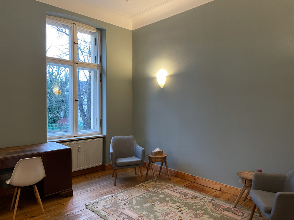 Mittelgroßes Nordisches Arbeitszimmer mit grüner Wandfarbe, braunem Holzboden, freistehendem Schreibtisch und braunem Boden in Berlin
