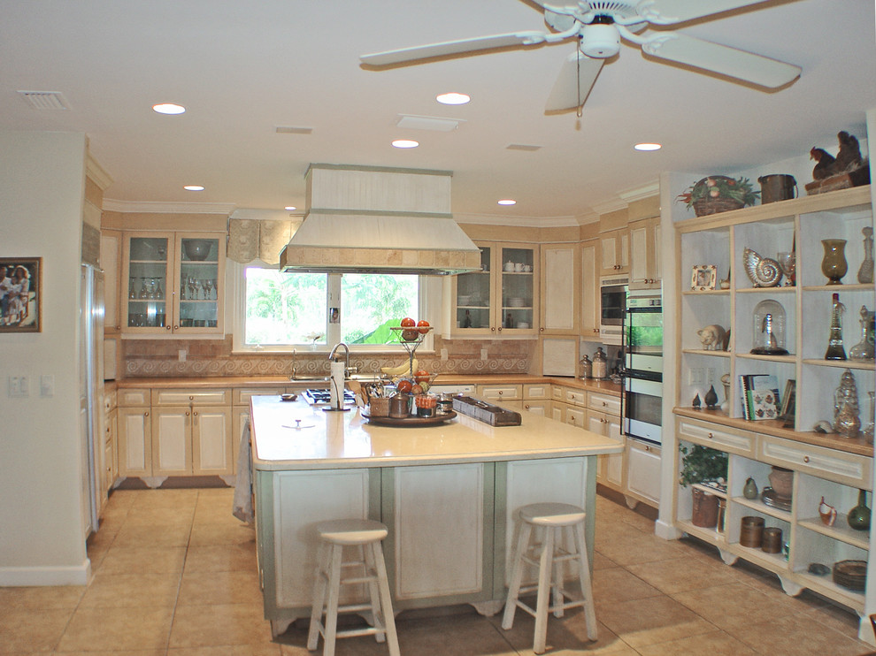Bild på ett stort lantligt kök, med en trippel diskho, luckor med infälld panel, skåp i slitet trä, marmorbänkskiva, gult stänkskydd, vita vitvaror, marmorgolv och en köksö