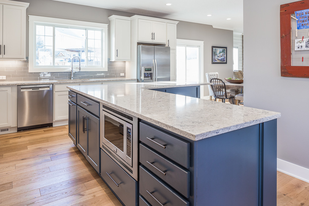 Large transitional l-shaped eat-in kitchen photo with white cabinets, quartzite countertops, gray backsplash, glass tile backsplash, stainless steel appliances and an island