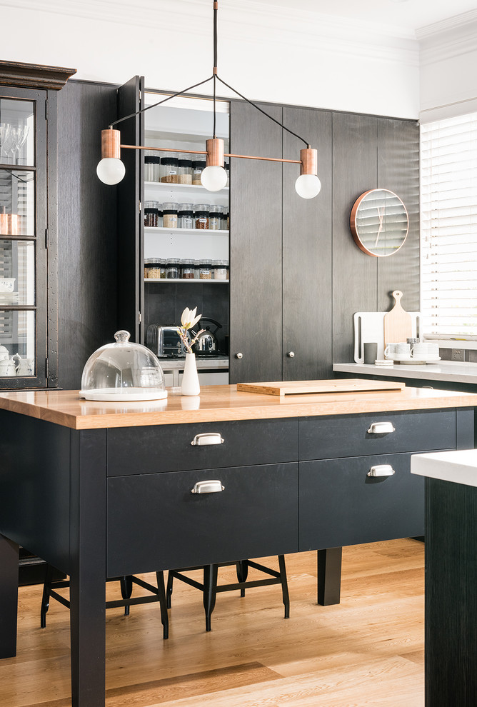 Design ideas for a large eclectic u-shaped kitchen pantry in Melbourne with an undermount sink, flat-panel cabinets, black cabinets, solid surface benchtops, grey splashback, black appliances, with island, ceramic splashback and light hardwood floors.