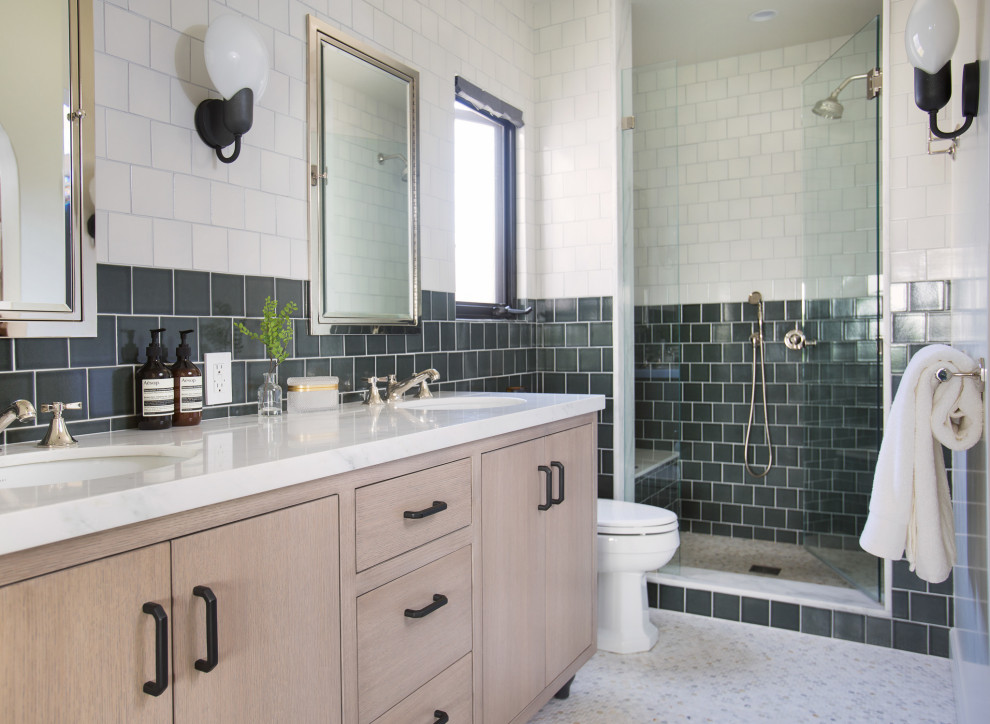 Photo of a mid-sized transitional master bathroom in Los Angeles with flat-panel cabinets, light wood cabinets, a one-piece toilet, green tile, engineered quartz benchtops, white floor, a hinged shower door, white benchtops, a shower seat, a double vanity, an alcove shower, an undermount sink and a freestanding vanity.