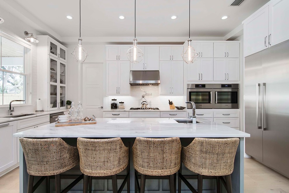 Inspiration for a large beach style u-shaped kitchen in Orlando with white cabinets, marble benchtops, white splashback, porcelain splashback, stainless steel appliances, light hardwood floors, with island, shaker cabinets, an undermount sink, beige floor and white benchtop.