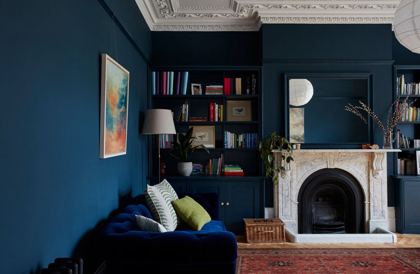Cette image montre un grand salon victorien avec un mur bleu, un sol en bois brun, une cheminée standard et un manteau de cheminée en pierre.