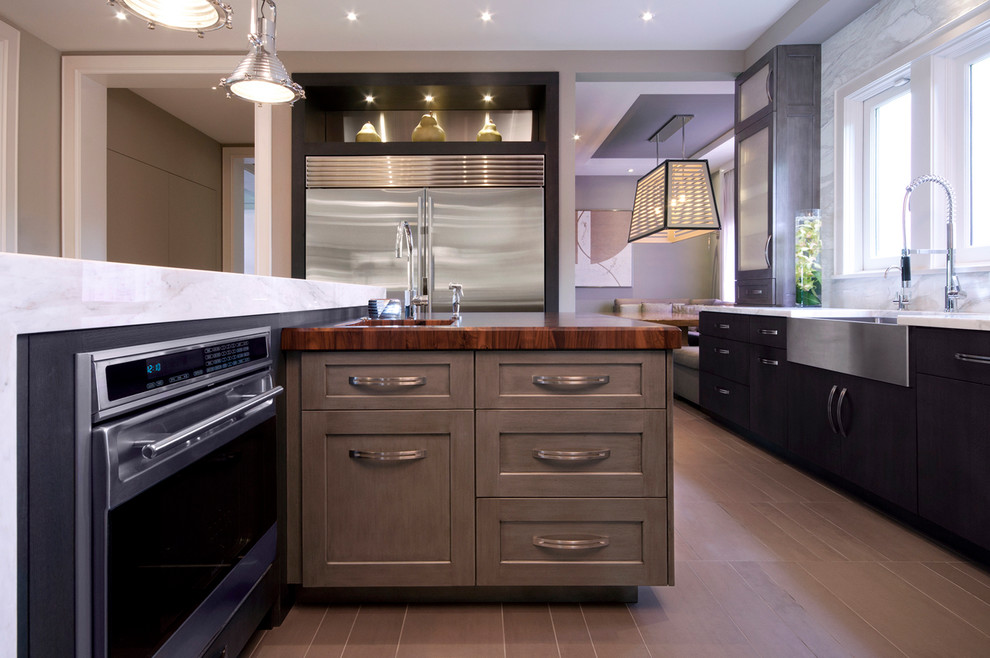Photo of a mid-sized traditional u-shaped eat-in kitchen in Miami with a farmhouse sink, stainless steel appliances, recessed-panel cabinets, dark wood cabinets, marble benchtops, light hardwood floors and with island.