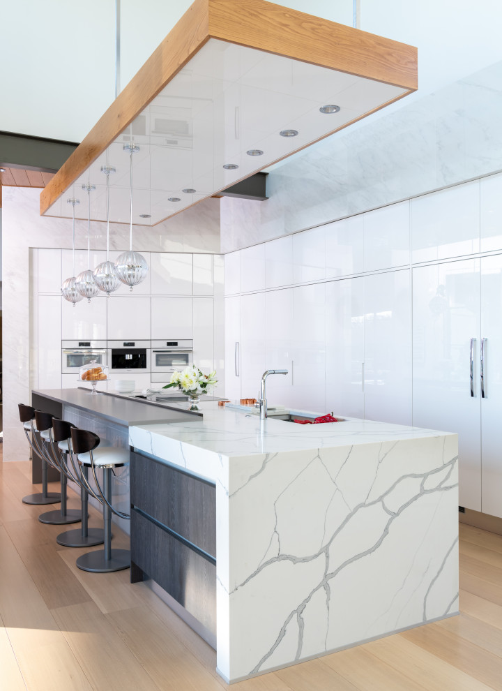 Inspiration for a contemporary l-shaped open plan kitchen in Dallas with an undermount sink, flat-panel cabinets, white cabinets, quartzite benchtops, panelled appliances, light hardwood floors, with island, beige floor and multi-coloured benchtop.