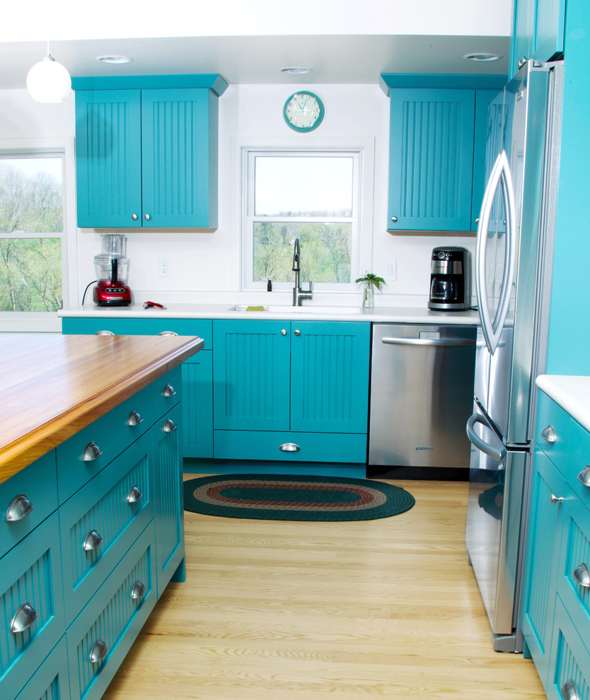 Inspiration for a mid-sized eclectic l-shaped eat-in kitchen in Milwaukee with an integrated sink, blue cabinets, wood benchtops, white splashback, stainless steel appliances, light hardwood floors, with island, flat-panel cabinets, brown floor and white benchtop.