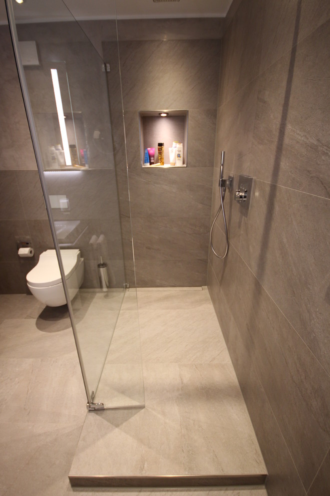 This is an example of a medium sized contemporary shower room bathroom in Cologne with a walk-in shower, a wall mounted toilet, grey tiles, stone tiles, grey walls, cement flooring, an integrated sink, grey floors and an open shower.