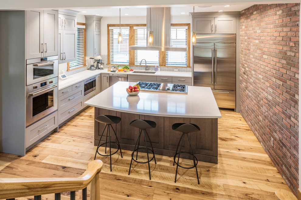 Large transitional l-shaped eat-in kitchen in Denver with an undermount sink, shaker cabinets, grey cabinets, stainless steel appliances, light hardwood floors and with island.
