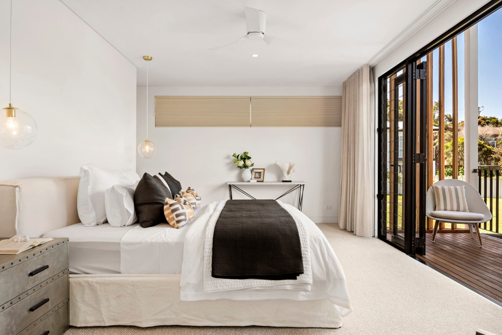 Large beach style master bedroom in Sydney with white walls, carpet and beige floor.