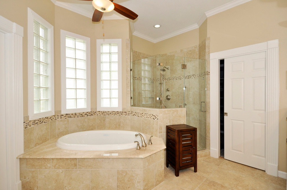 This is an example of a large traditional master bathroom in Houston with an undermount sink, raised-panel cabinets, white cabinets, a drop-in tub, an alcove shower, a one-piece toilet, beige tile and beige walls.