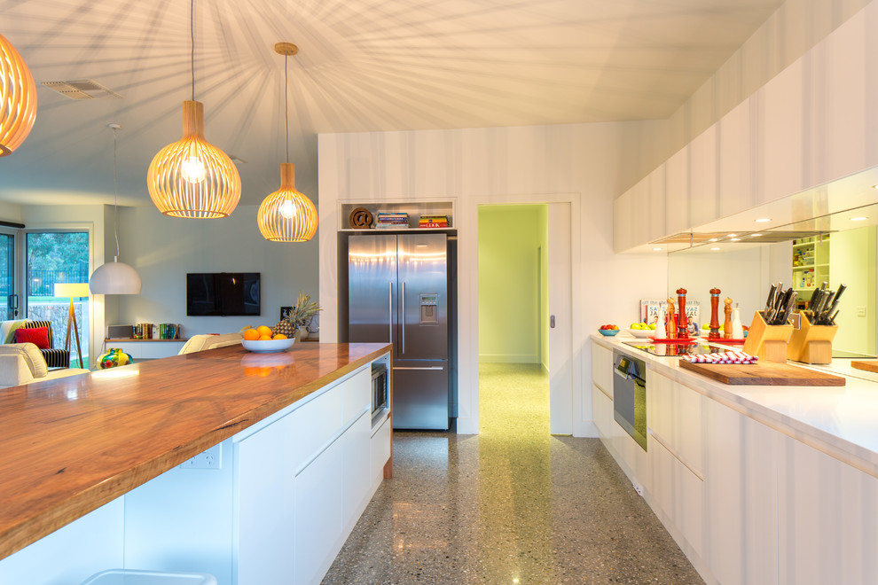 Contemporary u-shaped open plan kitchen in Melbourne with flat-panel cabinets, white cabinets, wood benchtops, metallic splashback, mirror splashback, stainless steel appliances and a peninsula.