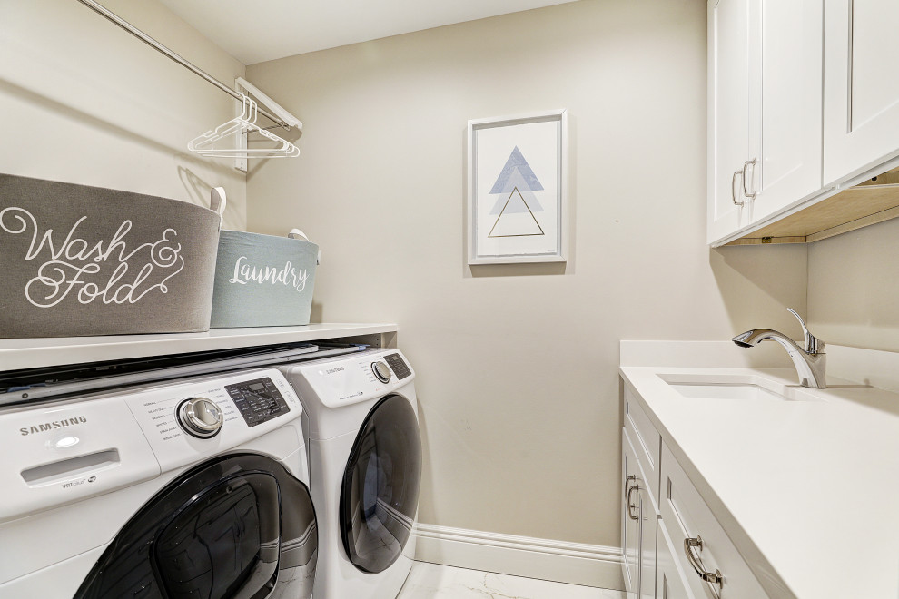 Photo of a small transitional galley dedicated laundry room in New York with an undermount sink, shaker cabinets, white cabinets, quartz benchtops, grey walls, ceramic floors, a side-by-side washer and dryer, white floor and white benchtop.