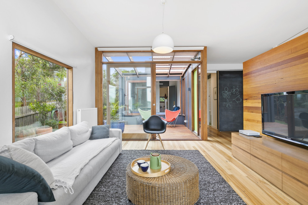 This is an example of a mid-sized contemporary open concept living room in Melbourne with white walls, light hardwood floors, a wall-mounted tv and planked wall panelling.