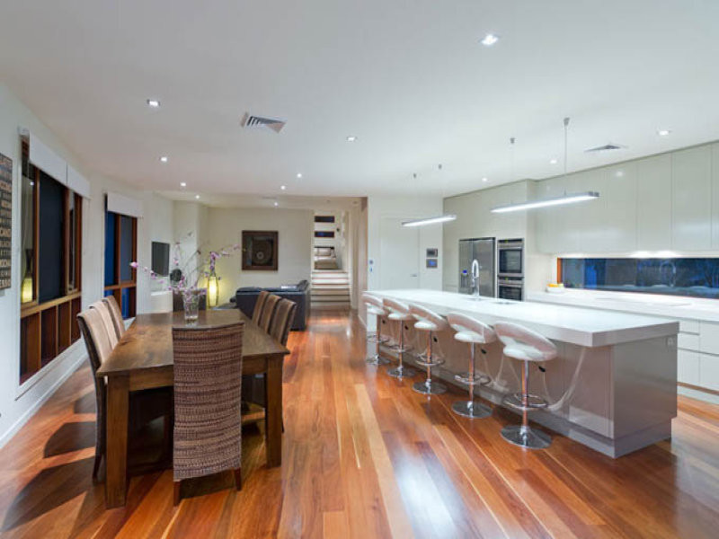 Mid-sized contemporary single-wall open plan kitchen in Brisbane with an undermount sink, flat-panel cabinets, white cabinets, solid surface benchtops, window splashback, stainless steel appliances, medium hardwood floors and with island.