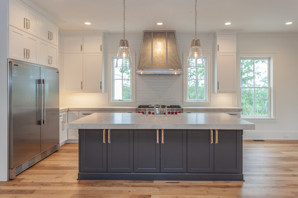 Inspiration for an expansive beach style l-shaped open plan kitchen in Charleston with a farmhouse sink, beaded inset cabinets, blue cabinets, quartzite benchtops, white splashback, subway tile splashback, stainless steel appliances, light hardwood floors, with island and white benchtop.
