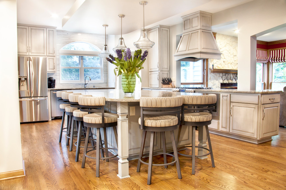 Design ideas for a large transitional l-shaped open plan kitchen in Milwaukee with an undermount sink, white cabinets, granite benchtops, grey splashback, stainless steel appliances, medium hardwood floors, with island and brown floor.
