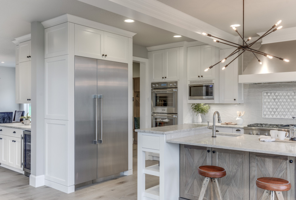 Design ideas for a large transitional u-shaped eat-in kitchen in Portland with a farmhouse sink, shaker cabinets, white cabinets, quartz benchtops, grey splashback, ceramic splashback, stainless steel appliances, light hardwood floors, with island, grey floor and white benchtop.