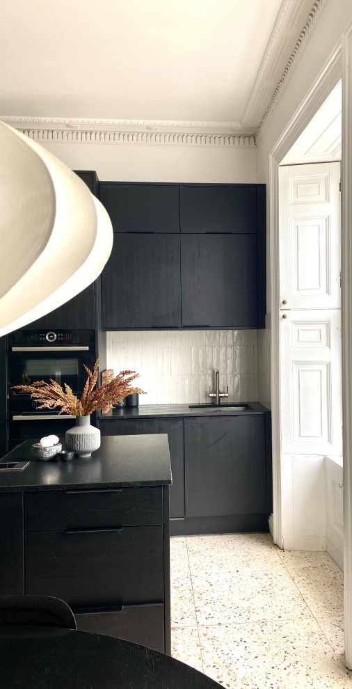 Photo of a large contemporary galley eat-in kitchen in Other with a single-bowl sink, flat-panel cabinets, dark wood cabinets, granite benchtops, white splashback, ceramic splashback, black appliances, terrazzo floors, with island, beige floor, black benchtop and wallpaper.