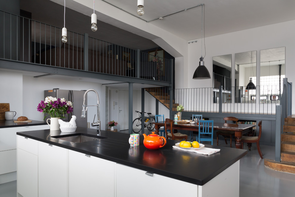 Inspiration for a large eclectic galley eat-in kitchen in London with an undermount sink, flat-panel cabinets, white cabinets, solid surface benchtops, white splashback, stone slab splashback, stainless steel appliances and with island.