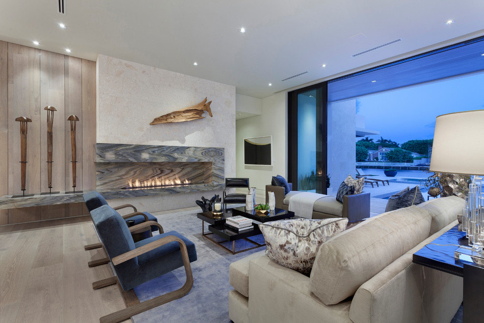This is an example of an expansive contemporary open concept living room in Miami with a home bar, white walls, light hardwood floors, a ribbon fireplace, a stone fireplace surround and no tv.