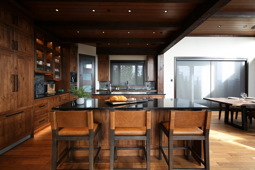 Large mountain style u-shaped medium tone wood floor, brown floor and exposed beam open concept kitchen photo with an undermount sink, shaker cabinets, medium tone wood cabinets, quartz countertops, gray backsplash, slate backsplash, stainless steel appliances, two islands and black countertops