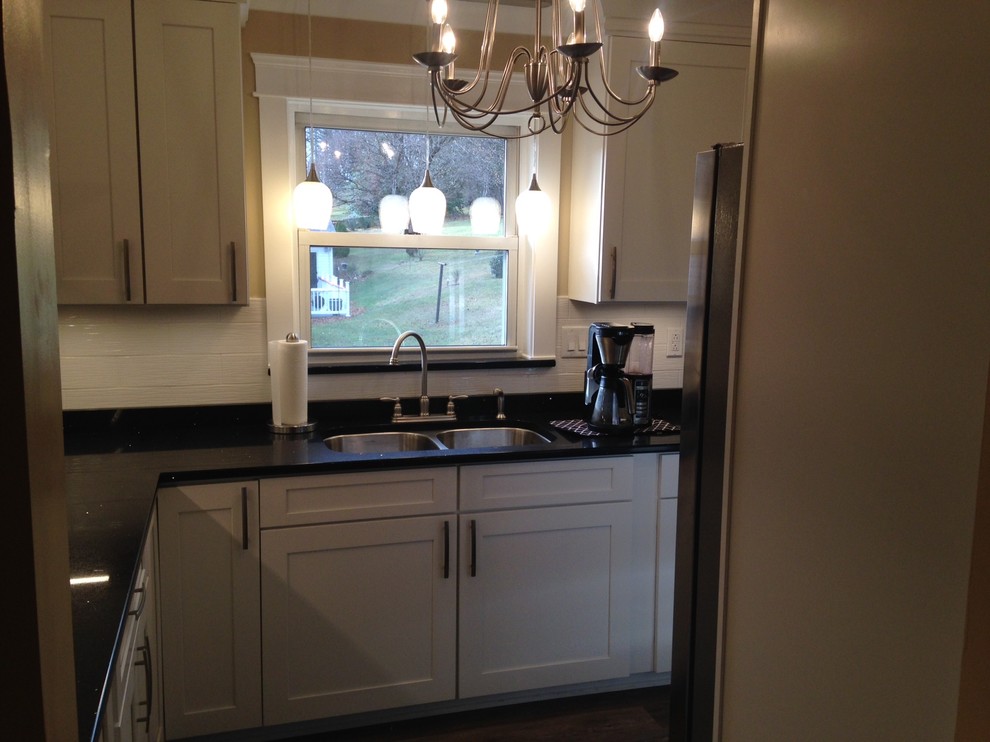 Mid-sized arts and crafts u-shaped vinyl floor home design photo with a double-bowl sink, shaker cabinets, white cabinets, quartz countertops, white backsplash, porcelain backsplash, stainless steel appliances and no island