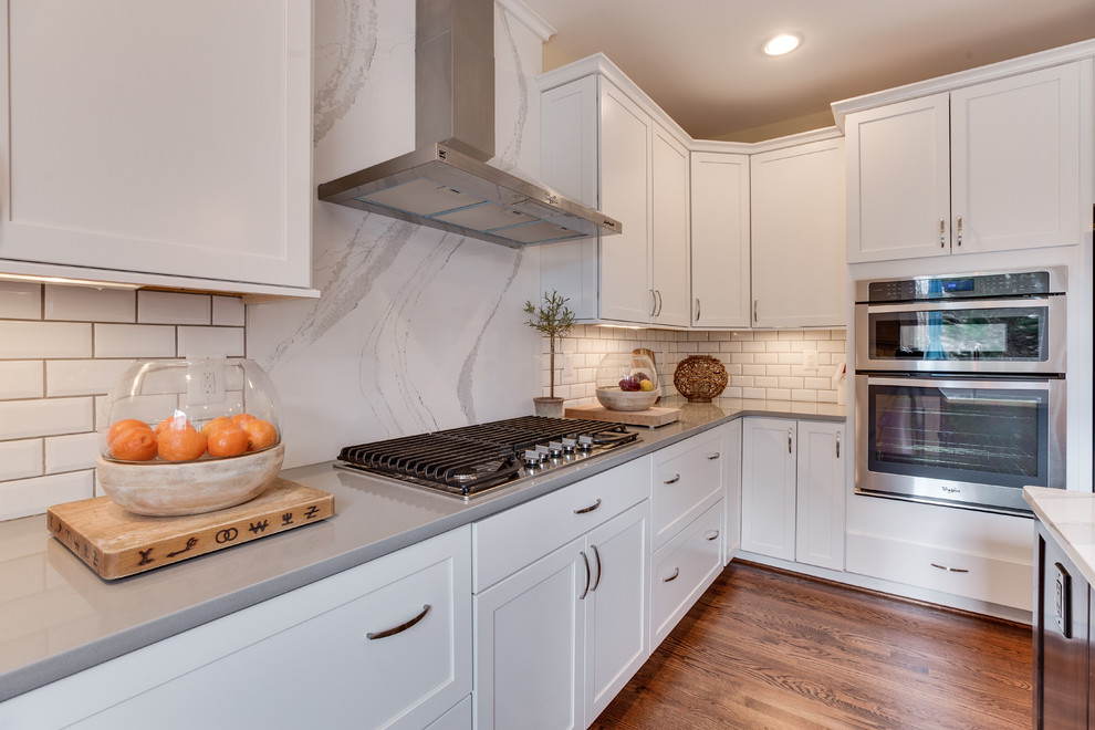 This is an example of a mid-sized contemporary u-shaped kitchen in DC Metro with an undermount sink, shaker cabinets, white cabinets, quartz benchtops, white splashback, stainless steel appliances, medium hardwood floors and with island.