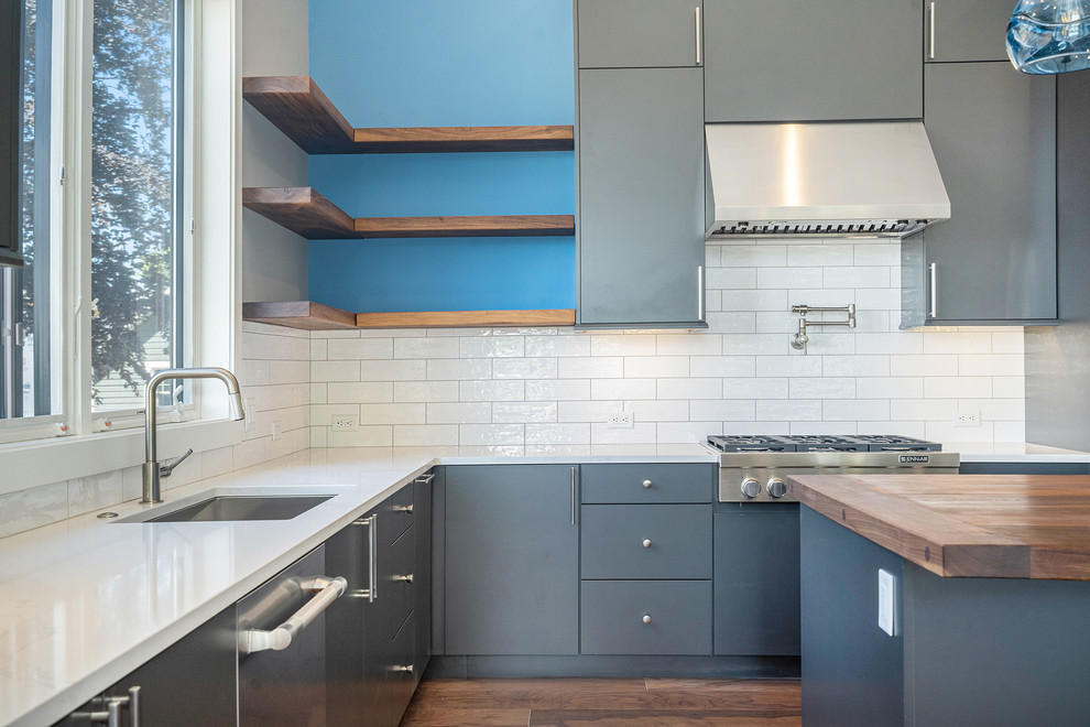 Mid-sized modern u-shaped eat-in kitchen in Grand Rapids with flat-panel cabinets, grey cabinets, quartz benchtops, white splashback, subway tile splashback, stainless steel appliances, medium hardwood floors, with island, brown floor, white benchtop and an undermount sink.