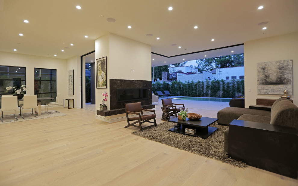 This is an example of an expansive contemporary formal open concept living room in Los Angeles with white walls, light hardwood floors, a stone fireplace surround, a wall-mounted tv and a ribbon fireplace.