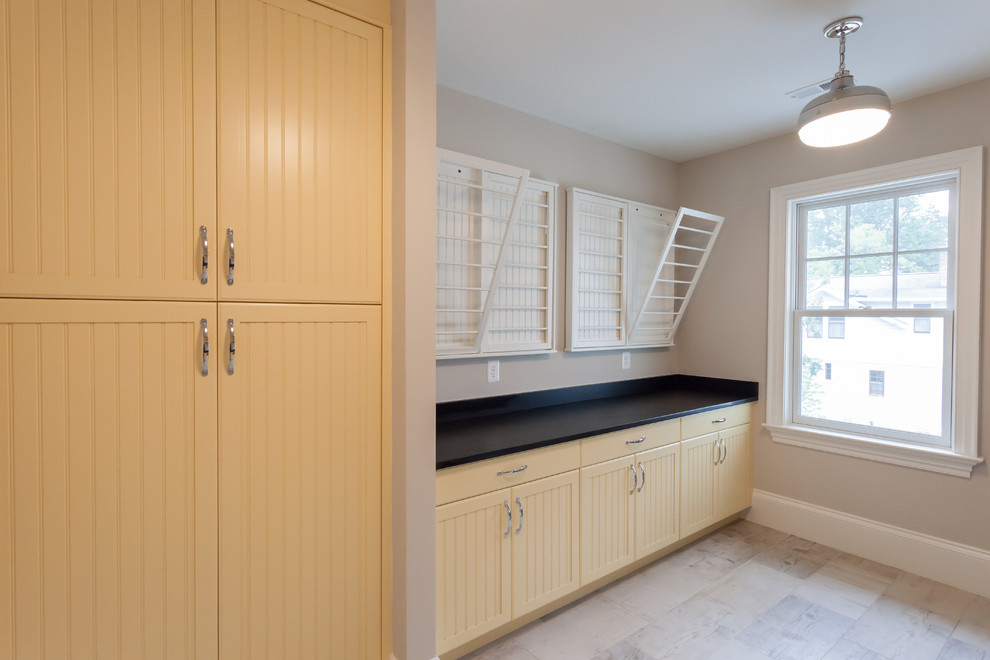 Inspiration for a country galley dedicated laundry room in DC Metro with a farmhouse sink, beaded inset cabinets, yellow cabinets, beige walls, a side-by-side washer and dryer, beige floor and black benchtop.