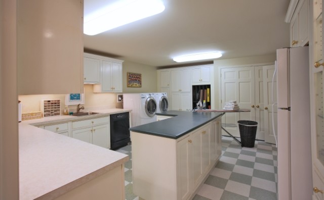 Photo of a large traditional u-shaped utility room in DC Metro with a drop-in sink, shaker cabinets, white cabinets, solid surface benchtops, beige walls, ceramic floors and a side-by-side washer and dryer.