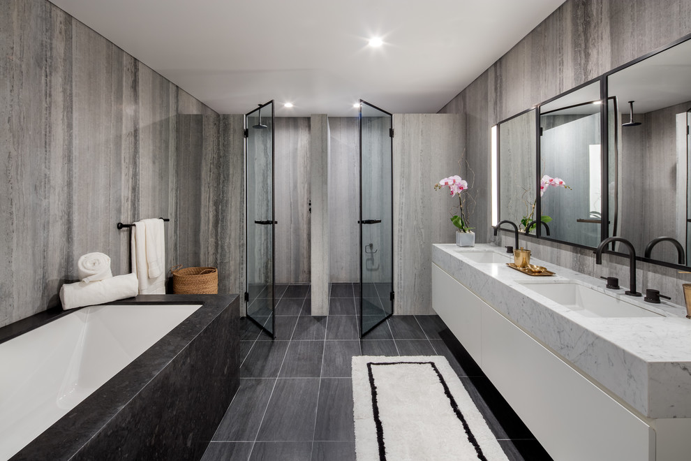 This is an example of a mid-sized contemporary master bathroom in New York with flat-panel cabinets, white cabinets, stone slab, grey walls, slate floors, an undermount sink, marble benchtops, grey floor, an undermount tub, a corner shower and a hinged shower door.