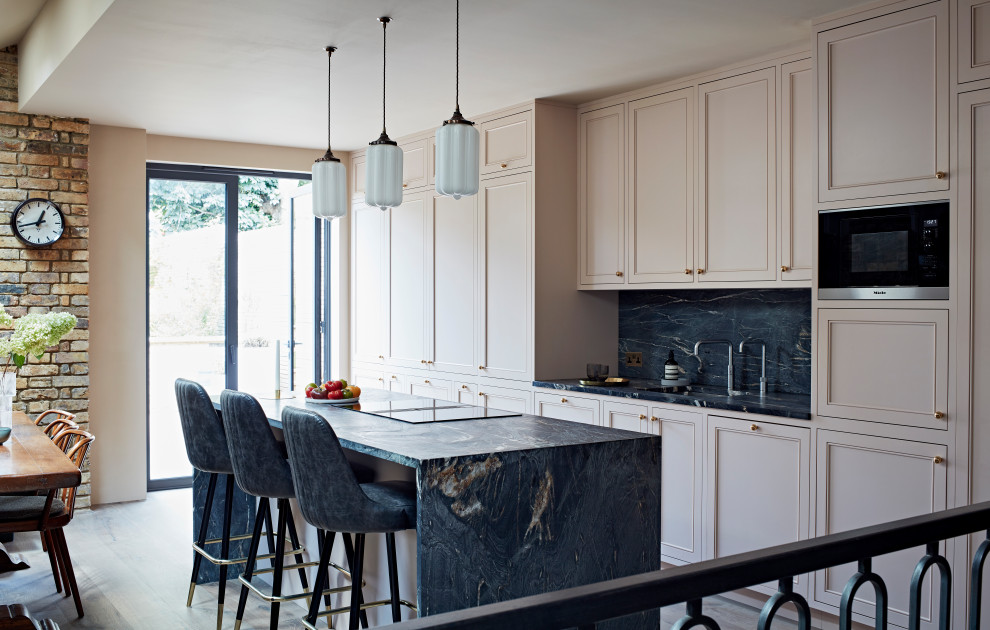 Contemporary galley eat-in kitchen in London with an integrated sink, recessed-panel cabinets, pink cabinets, marble benchtops, black splashback, marble splashback, light hardwood floors, with island and black benchtop.