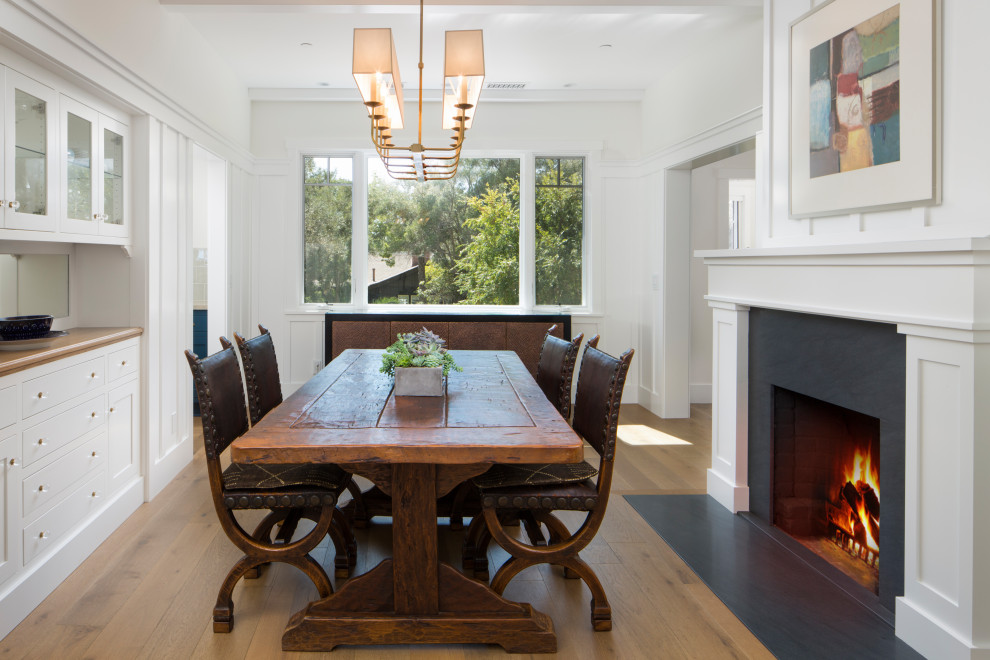 Inspiration for a beach style dining room in Santa Barbara with white walls, medium hardwood floors, a standard fireplace, a wood fireplace surround and brown floor.